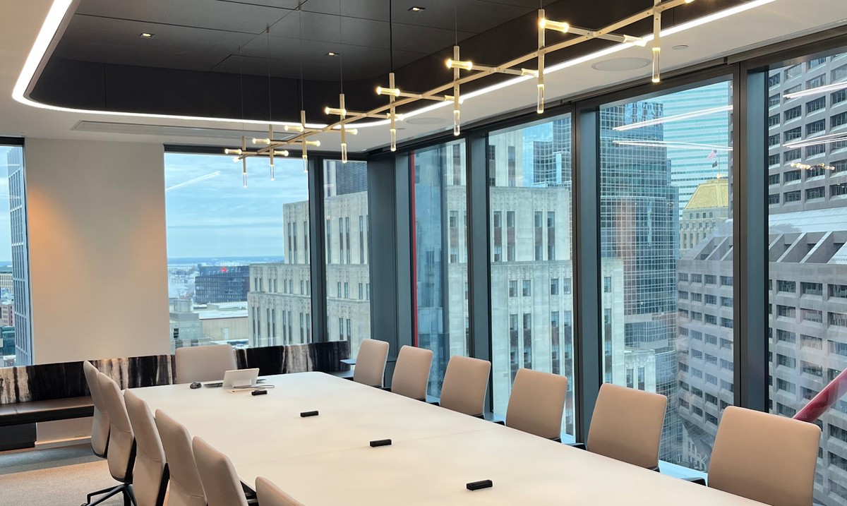 Corporate boardroom with suspended LED cove lighting, recessed ceiling downlights, a brass fixture over the table, and built-in tabletop power modules
