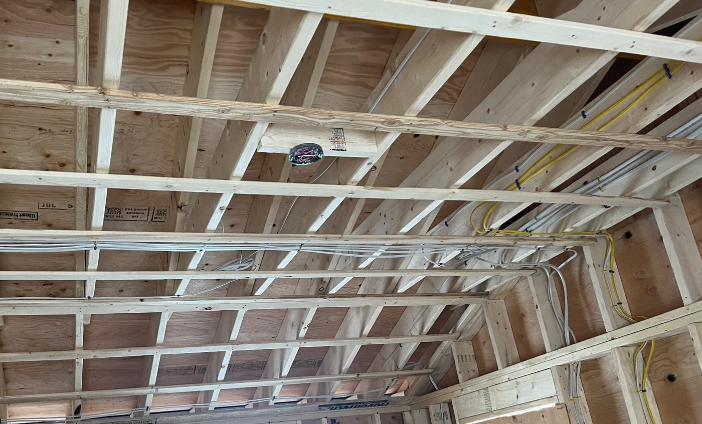 Open wood stud and ceiling framing on a new build with neatly stapled Romex runs and a centered ceiling junction box