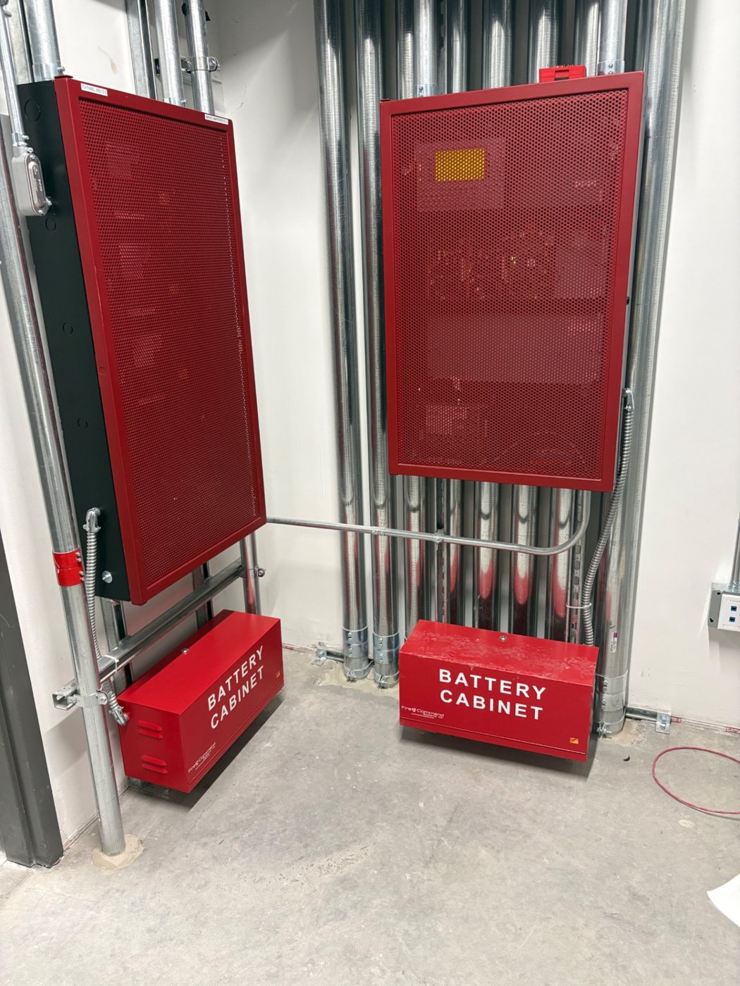 Fire alarm power panels with battery cabinets and EMT conduit runs in a utility room