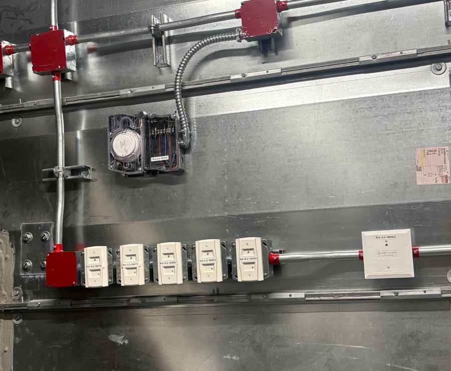 Notifier fire alarm monitor modules, red junction boxes and conduit installed on an air handling unit in a mechanical room