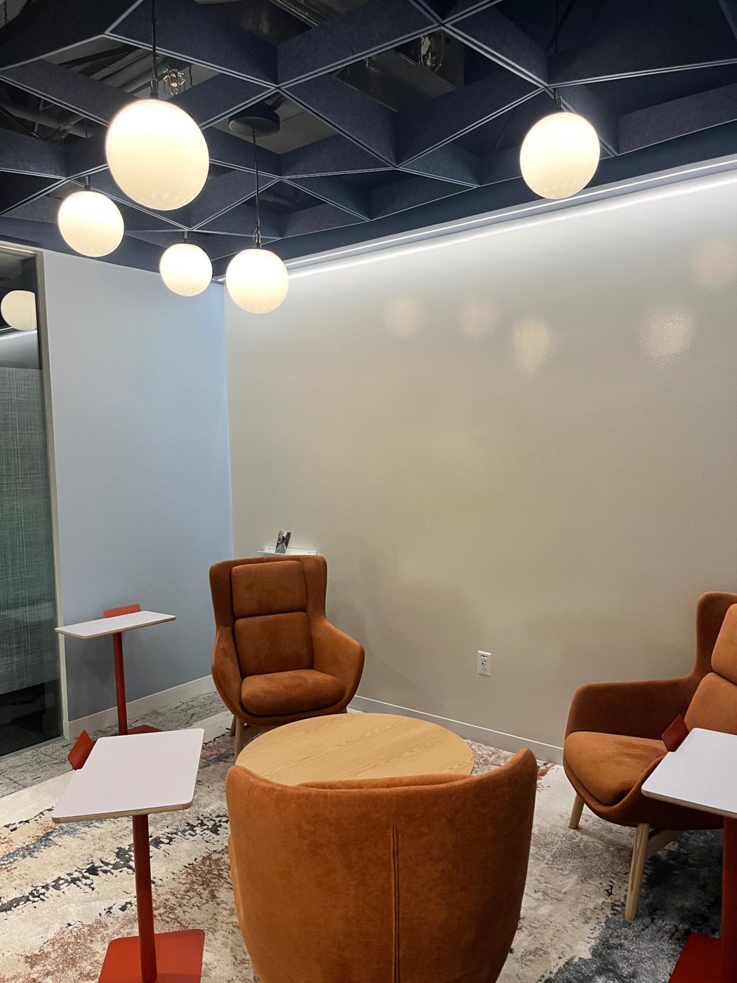 Cluster of globe pendants and linear LED wall-wash in an office lounge with acoustic ceiling