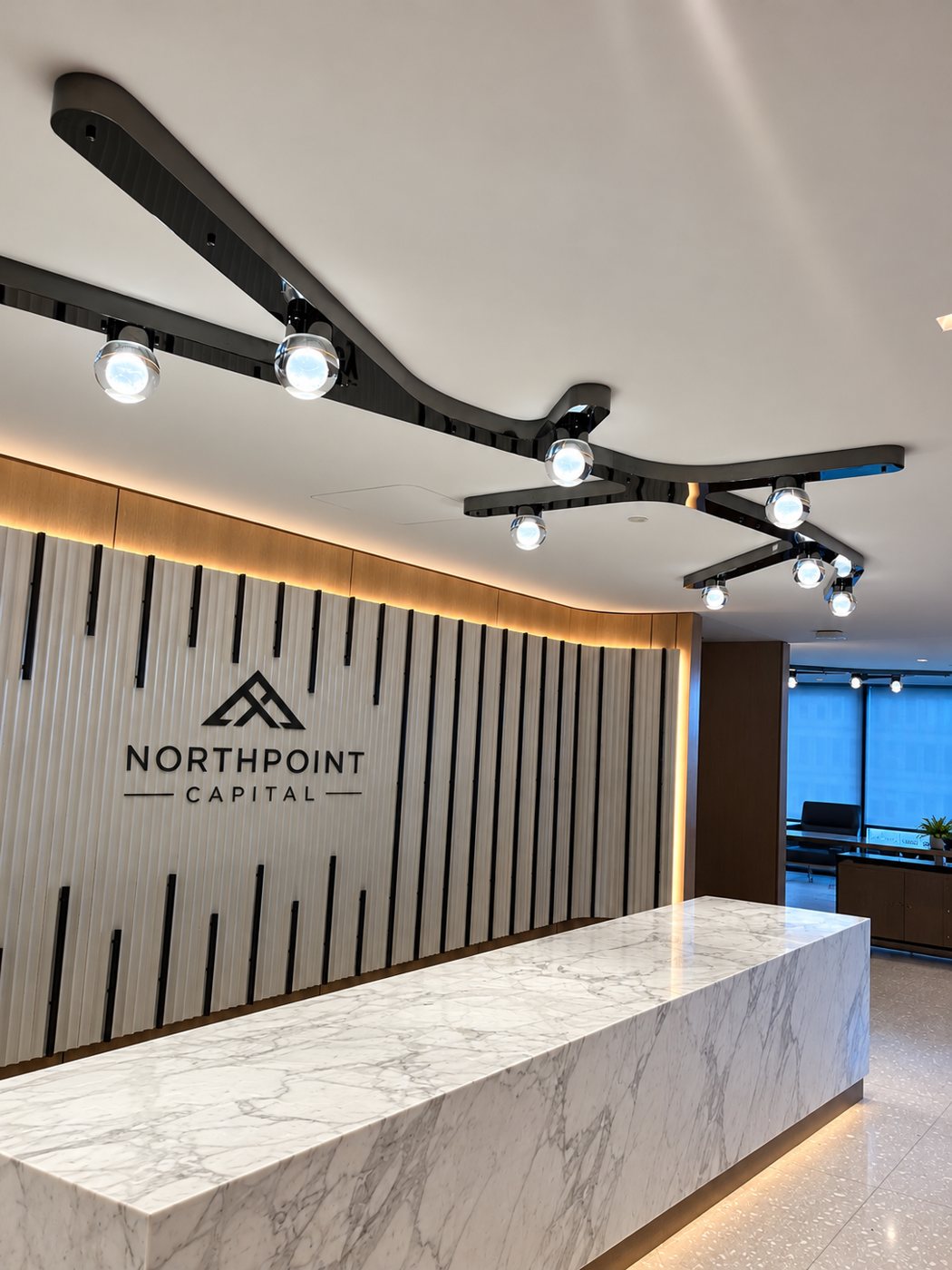 Branching black track lighting and LED wall-wash above a marble reception desk